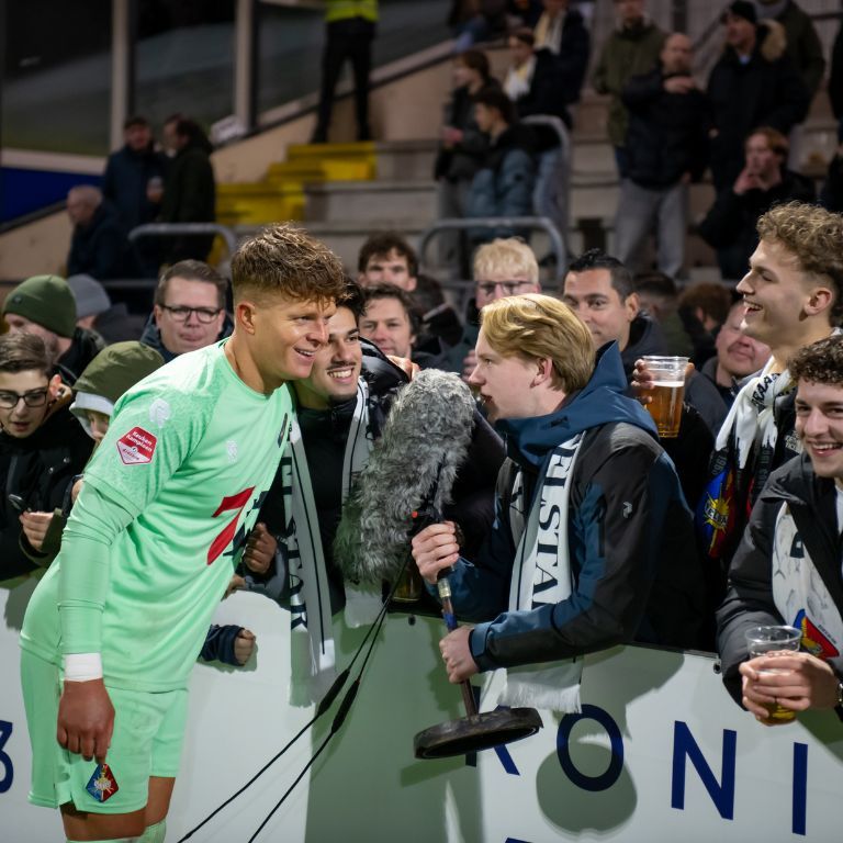 Telstar-doelman in groen tenue in gesprek met supporters langs de tribune van BUKO Stadion